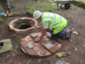 Alan assembling John B's well cover: mended well in the background, chain pump platform bases around it